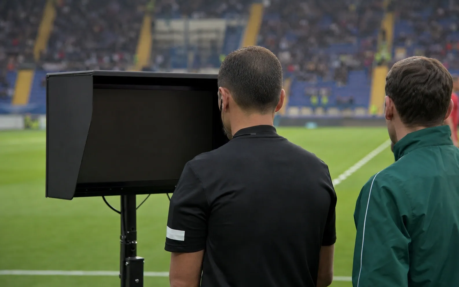 Ofisial pertandingan melihat monitor review kosong dari belakang di sisi lapangan