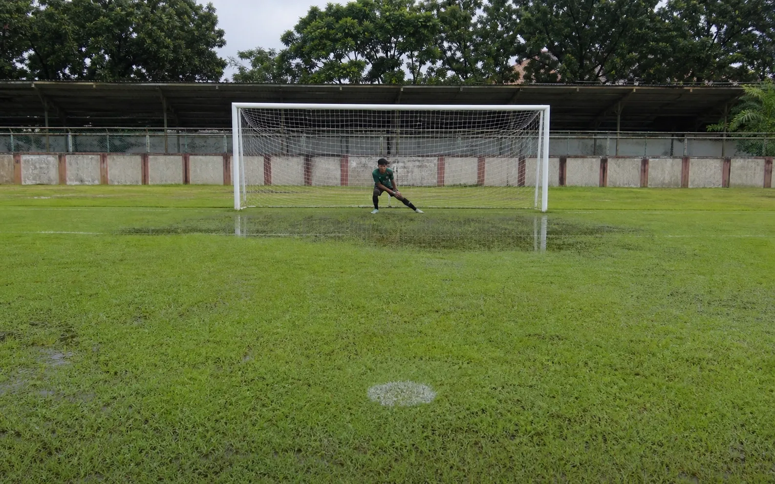Titik penalti dan gawang basah setelah hujan dengan kiper melakukan pemanasan